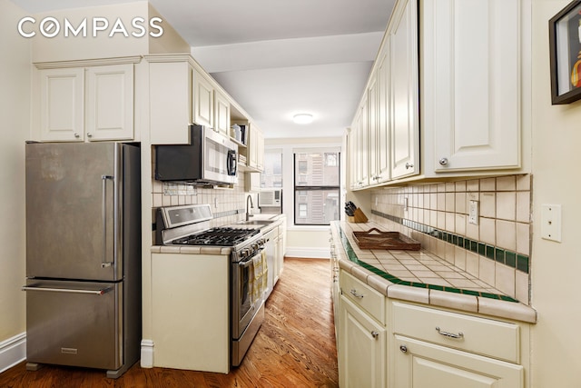 kitchen featuring tile counters, wood finished floors, stainless steel appliances, and a sink