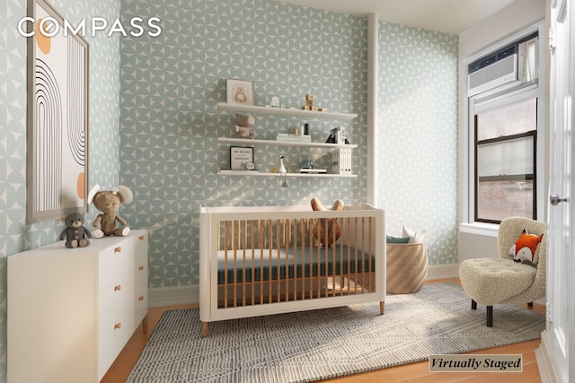 bedroom featuring wallpapered walls, a wall unit AC, a nursery area, and baseboards