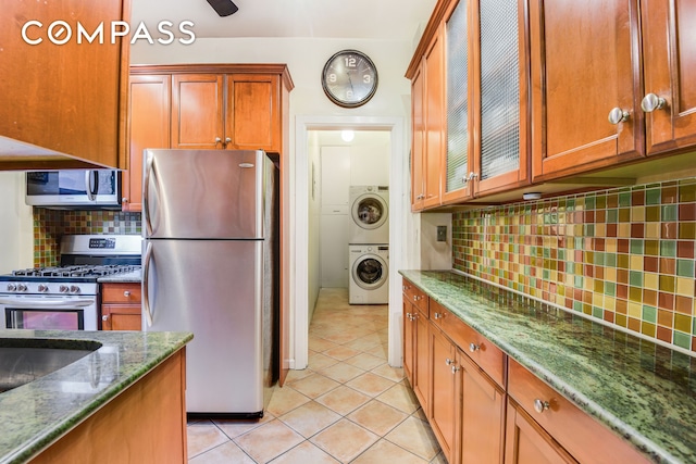 kitchen featuring dark stone countertops, light tile patterned flooring, glass insert cabinets, appliances with stainless steel finishes, and backsplash