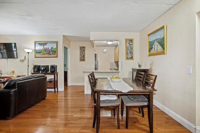 dining room featuring baseboards, light wood-style floors, and a textured ceiling