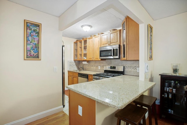 kitchen featuring backsplash, glass insert cabinets, a breakfast bar, a peninsula, and stainless steel appliances