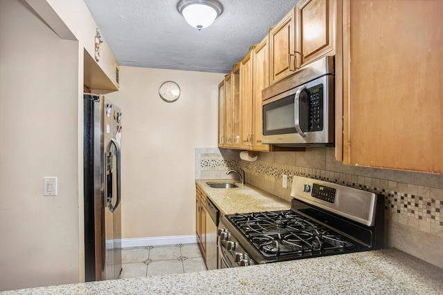 kitchen featuring baseboards, a sink, decorative backsplash, appliances with stainless steel finishes, and a textured ceiling