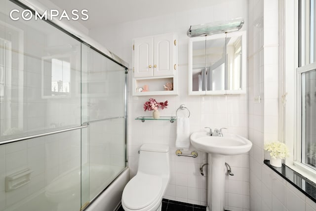 full bathroom with tile walls, toilet, enclosed tub / shower combo, and a sink