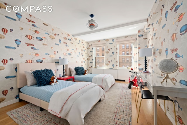 bedroom featuring beamed ceiling, wallpapered walls, wood finished floors, and baseboards