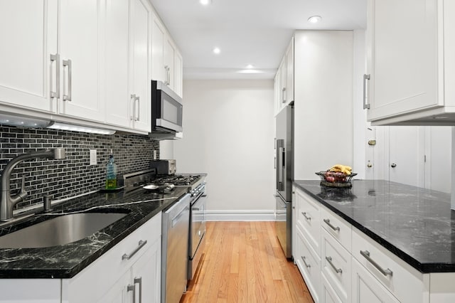 kitchen featuring a sink, stainless steel appliances, white cabinets, light wood-type flooring, and backsplash