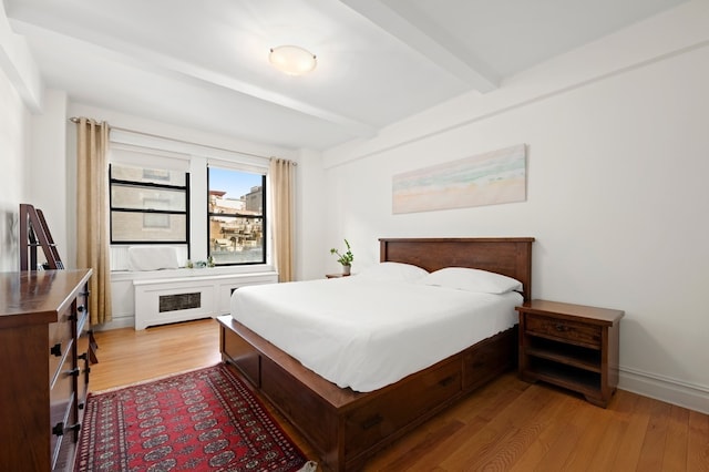 bedroom with beam ceiling, radiator, baseboards, and wood finished floors