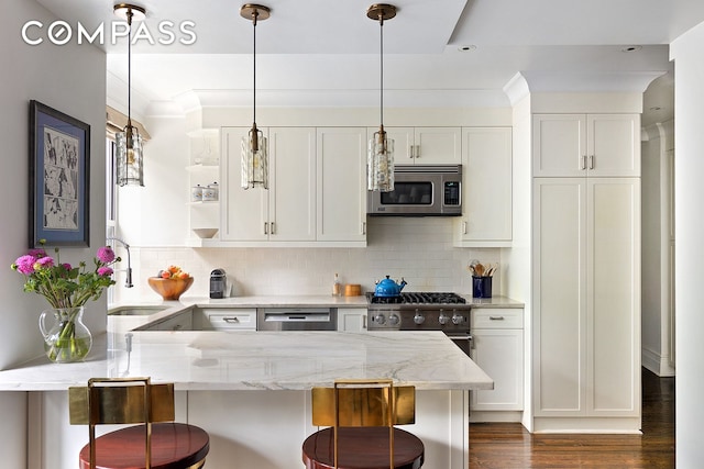 kitchen featuring a peninsula, a sink, stainless steel appliances, white cabinetry, and a kitchen breakfast bar