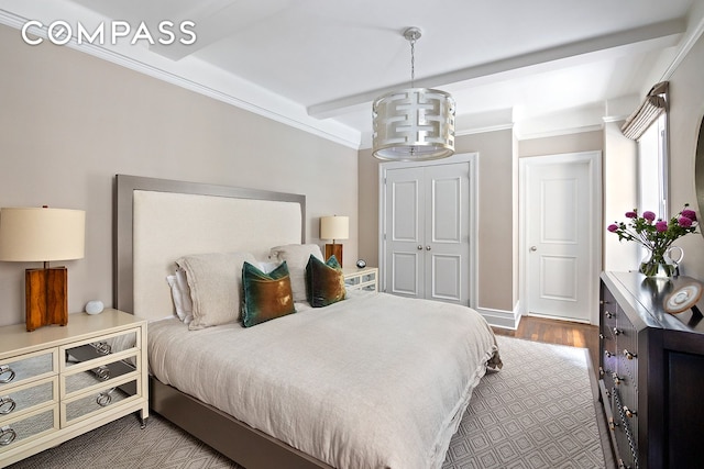 bedroom with beamed ceiling, ornamental molding, wood finished floors, a closet, and a chandelier