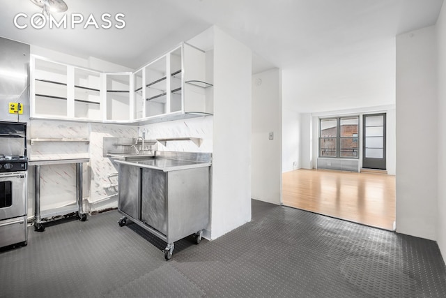 kitchen with open shelves, stainless steel counters, a sink, backsplash, and stainless steel range with gas stovetop