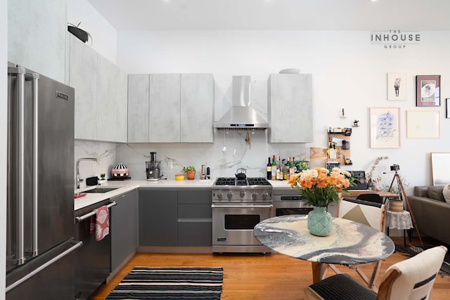 kitchen with tasteful backsplash, wall chimney range hood, light countertops, appliances with stainless steel finishes, and a sink