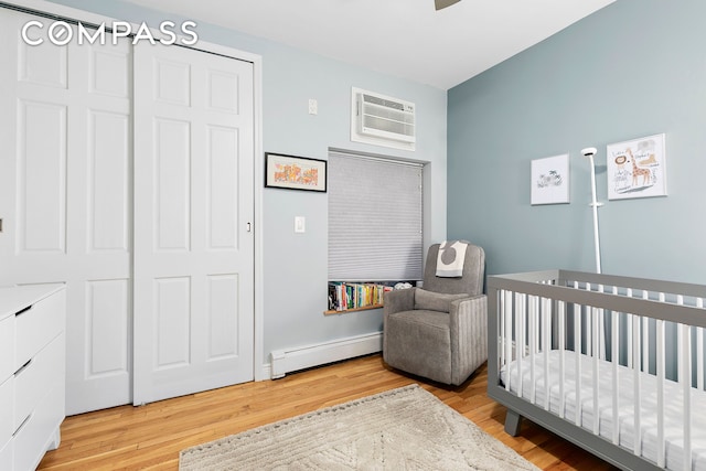 bedroom featuring light wood-type flooring, a baseboard heating unit, a nursery area, and a wall unit AC