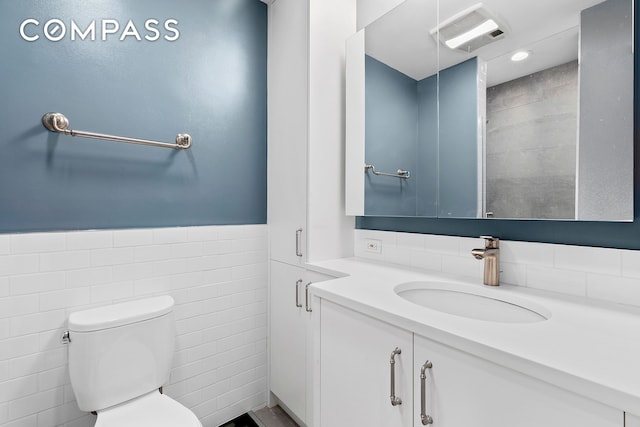 bathroom featuring vanity, visible vents, wainscoting, tile walls, and toilet