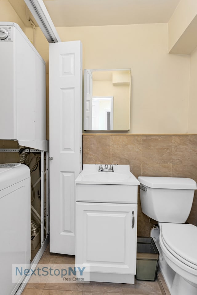 half bathroom featuring toilet, tile patterned flooring, vanity, washer / clothes dryer, and a wainscoted wall