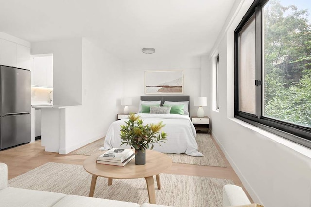 bedroom featuring baseboards, freestanding refrigerator, and light wood-style floors