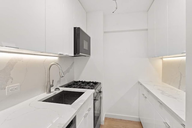 kitchen with modern cabinets, tasteful backsplash, white cabinetry, black microwave, and light stone countertops