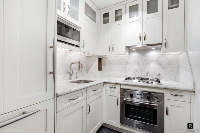 kitchen featuring a sink, under cabinet range hood, appliances with stainless steel finishes, white cabinets, and decorative backsplash