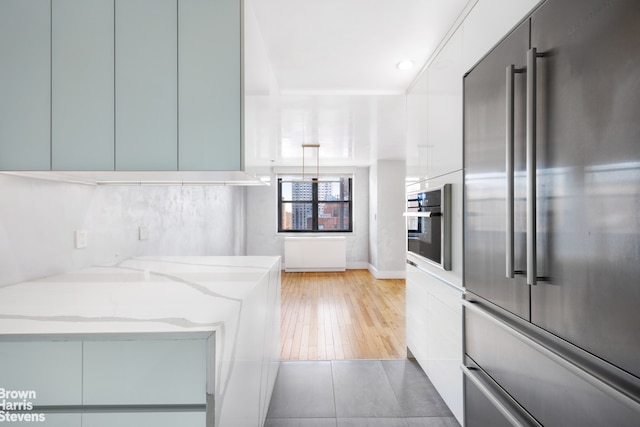 kitchen with light stone counters, appliances with stainless steel finishes, light wood-style floors, white cabinets, and modern cabinets