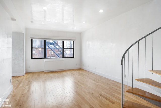 empty room with baseboards, hardwood / wood-style floors, stairs, and radiator heating unit