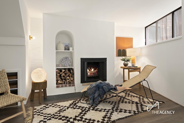 sitting room featuring built in shelves, wood finished floors, and a warm lit fireplace