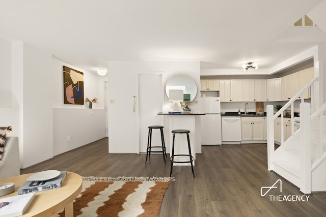 kitchen with dark wood-type flooring, a breakfast bar, dark countertops, white cabinetry, and white appliances