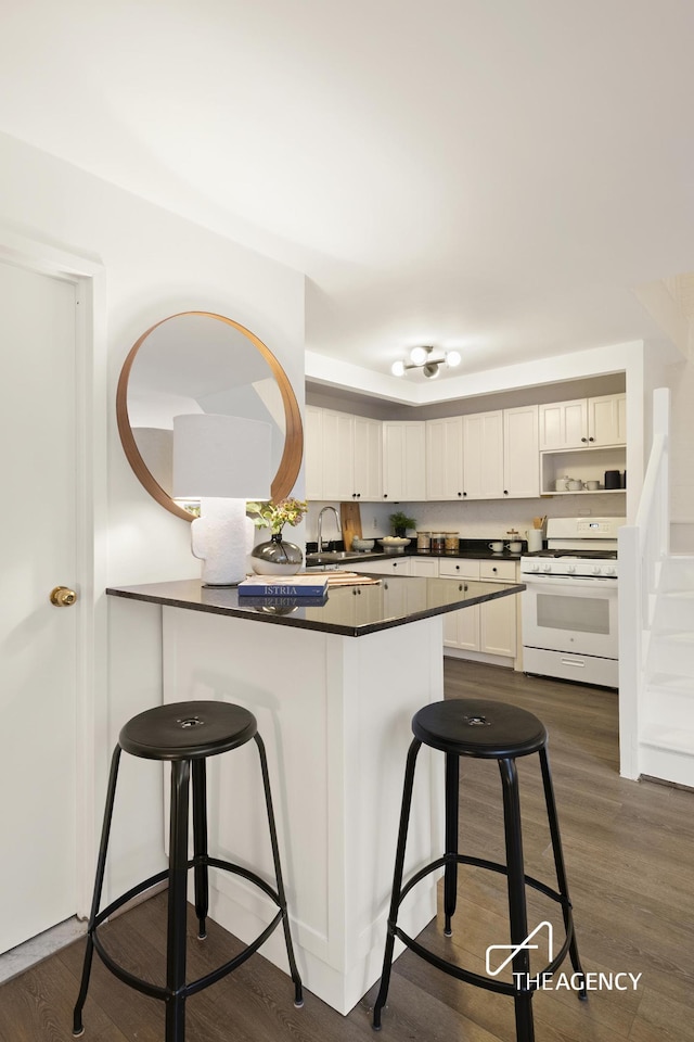 kitchen with a kitchen bar, gas range gas stove, dark countertops, a peninsula, and white cabinets