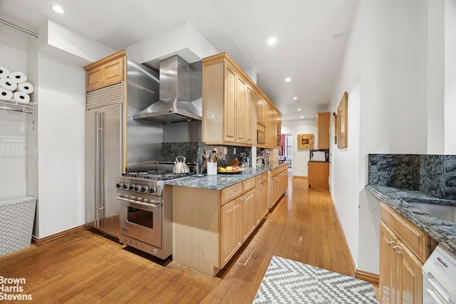 kitchen with light brown cabinets, wall chimney range hood, high quality appliances, decorative backsplash, and light wood-style floors