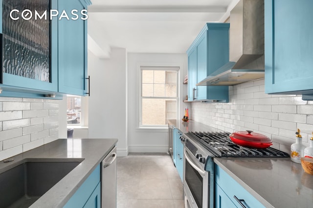 kitchen featuring light tile patterned floors, blue cabinetry, stainless steel appliances, and wall chimney range hood