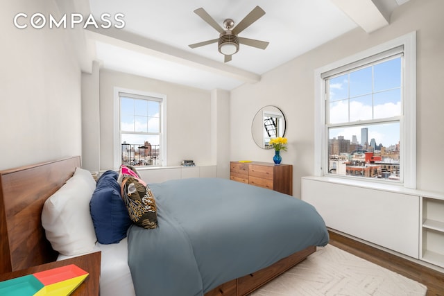 bedroom with ceiling fan, beamed ceiling, a city view, and wood finished floors