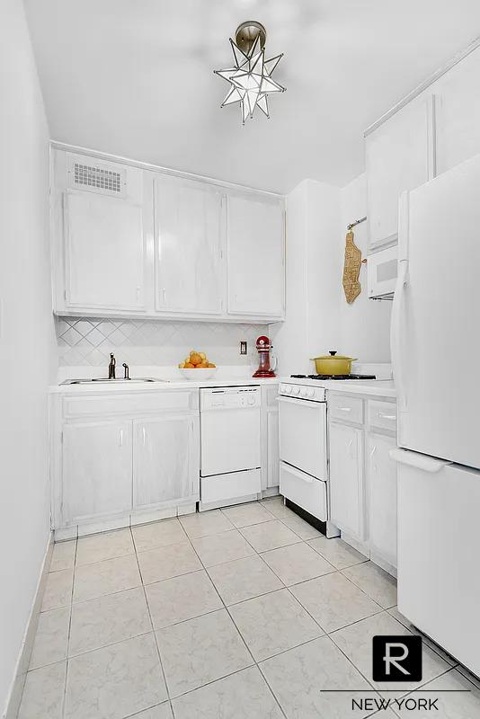 kitchen featuring white appliances, light countertops, visible vents, and a sink