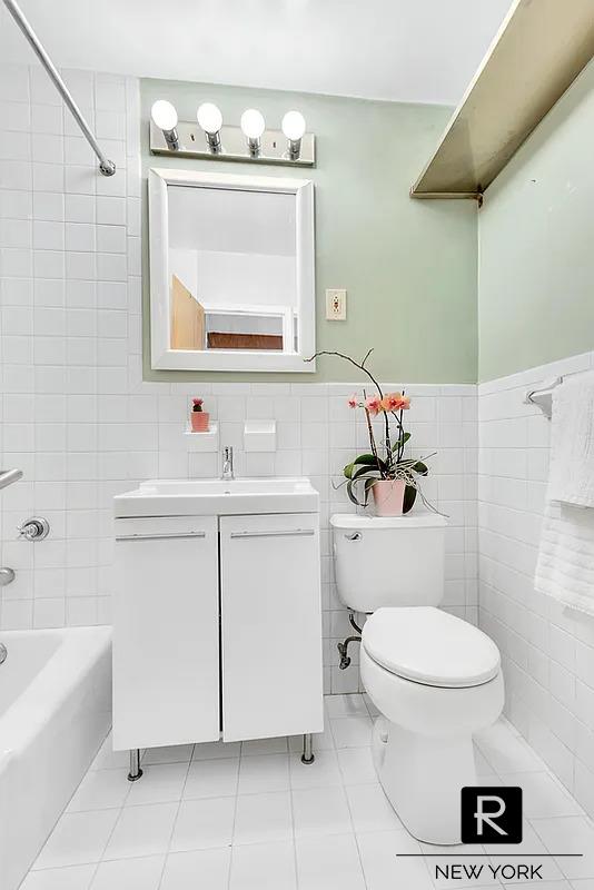 bathroom with toilet, tile walls, wainscoting, washtub / shower combination, and vanity