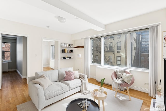 living room featuring beamed ceiling, baseboards, and light wood-style flooring