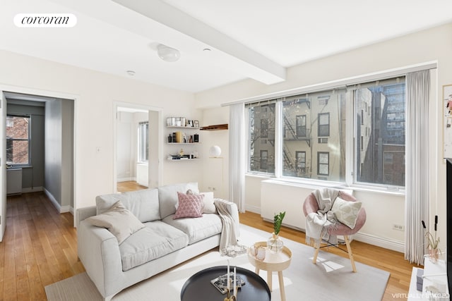 living area featuring visible vents, beam ceiling, light wood-style floors, and baseboards