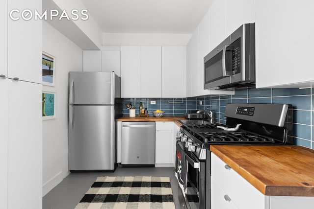 kitchen with stainless steel appliances, tasteful backsplash, butcher block counters, and white cabinetry