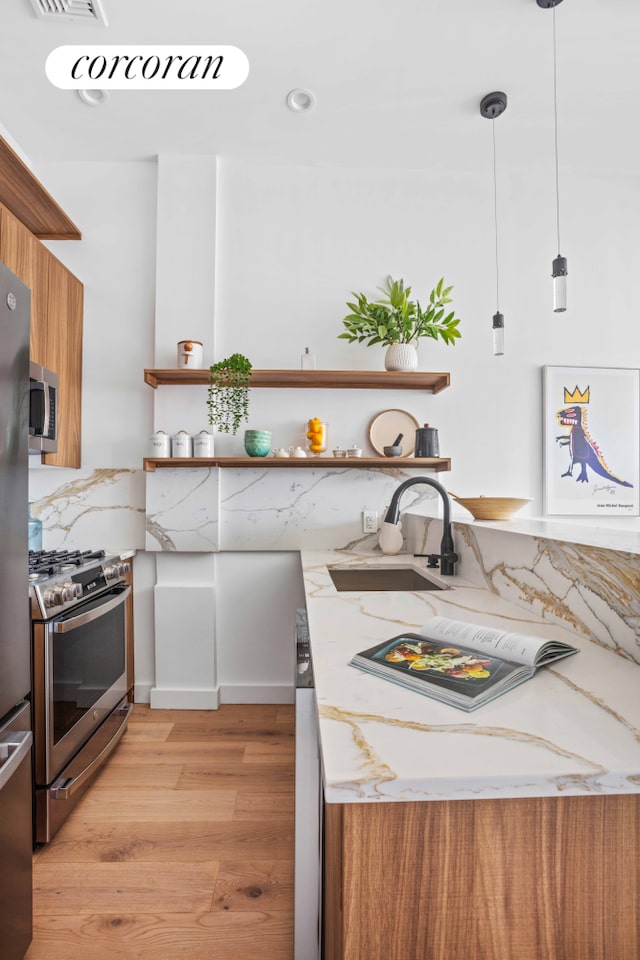 kitchen with open shelves, a sink, stainless steel appliances, light wood-style floors, and brown cabinetry