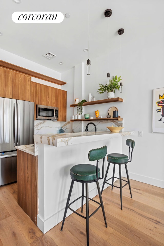 kitchen featuring visible vents, a kitchen bar, brown cabinets, appliances with stainless steel finishes, and modern cabinets