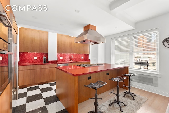 kitchen with light floors, a breakfast bar, appliances with stainless steel finishes, island range hood, and a sink