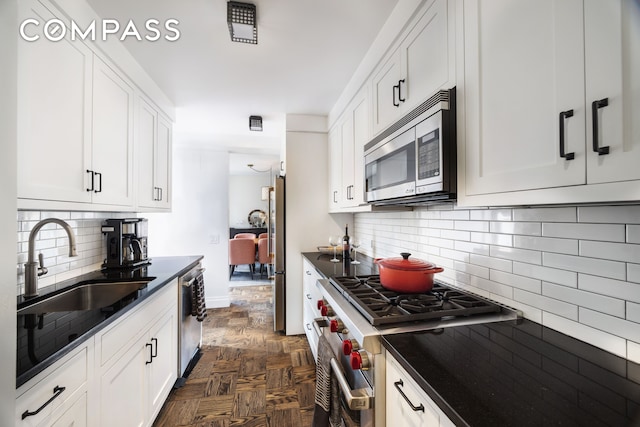 kitchen featuring dark countertops, white cabinetry, stainless steel appliances, and a sink