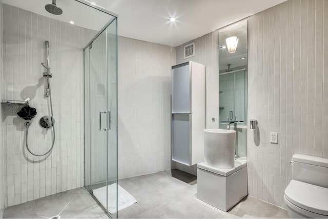 bathroom with tile walls, toilet, visible vents, and a stall shower