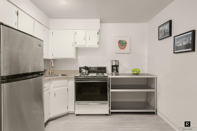 kitchen with light countertops, freestanding refrigerator, stove, white cabinets, and a sink