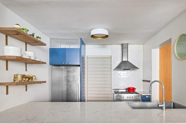 kitchen featuring open shelves, wall chimney range hood, light stone counters, premium appliances, and a sink