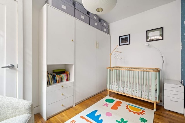 bedroom featuring a nursery area, wood finished floors, and a closet