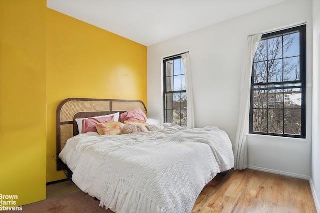 bedroom with multiple windows, baseboards, and wood finished floors