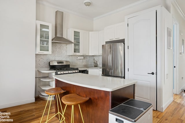 kitchen featuring wall chimney range hood, white cabinets, ornamental molding, and appliances with stainless steel finishes