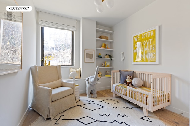 bedroom with a nursery area, wood finished floors, and baseboards