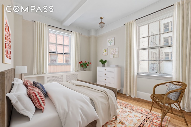 bedroom with beamed ceiling, baseboards, and light wood finished floors