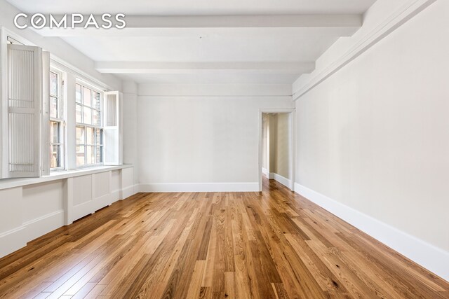 empty room featuring beam ceiling, baseboards, and wood-type flooring