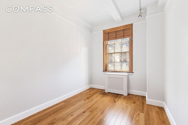 empty room with beam ceiling, light wood-type flooring, and baseboards