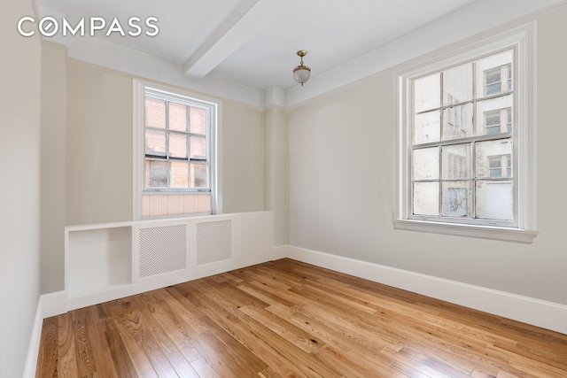 spare room featuring beam ceiling, baseboards, and light wood finished floors