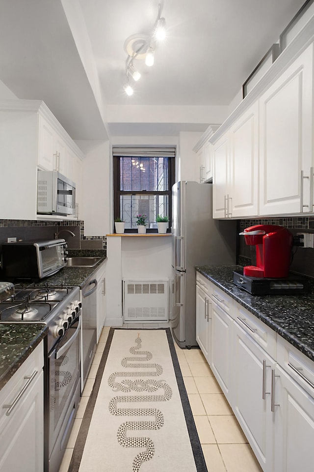 kitchen with a sink, tasteful backsplash, appliances with stainless steel finishes, white cabinets, and light tile patterned flooring