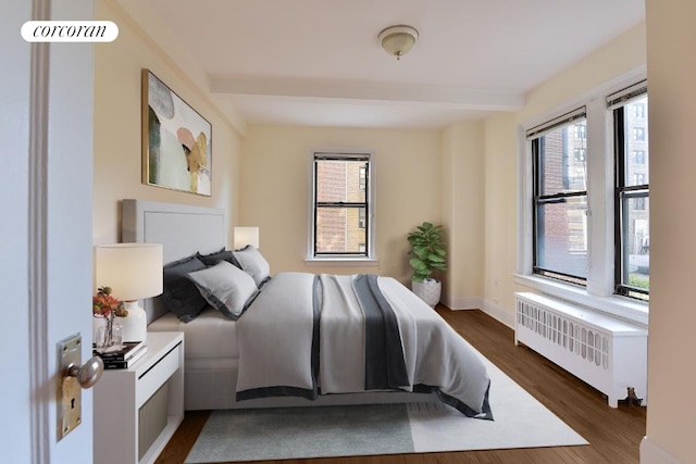 bedroom with baseboards, beam ceiling, dark wood-style flooring, and radiator heating unit